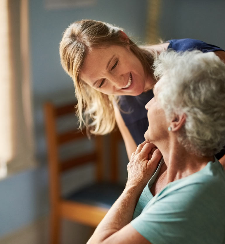 Caregiver smiling at senior woman in a home setting, showing compassionate memory care.
