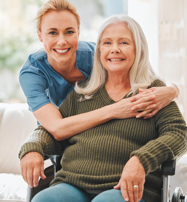 Caregiver hugging a smiling senior woman in a wheelchair, both looking happy and content.