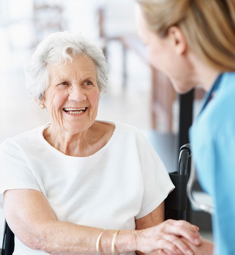 Elderly woman smiling at a caregiver in a blue uniform while holding hands
