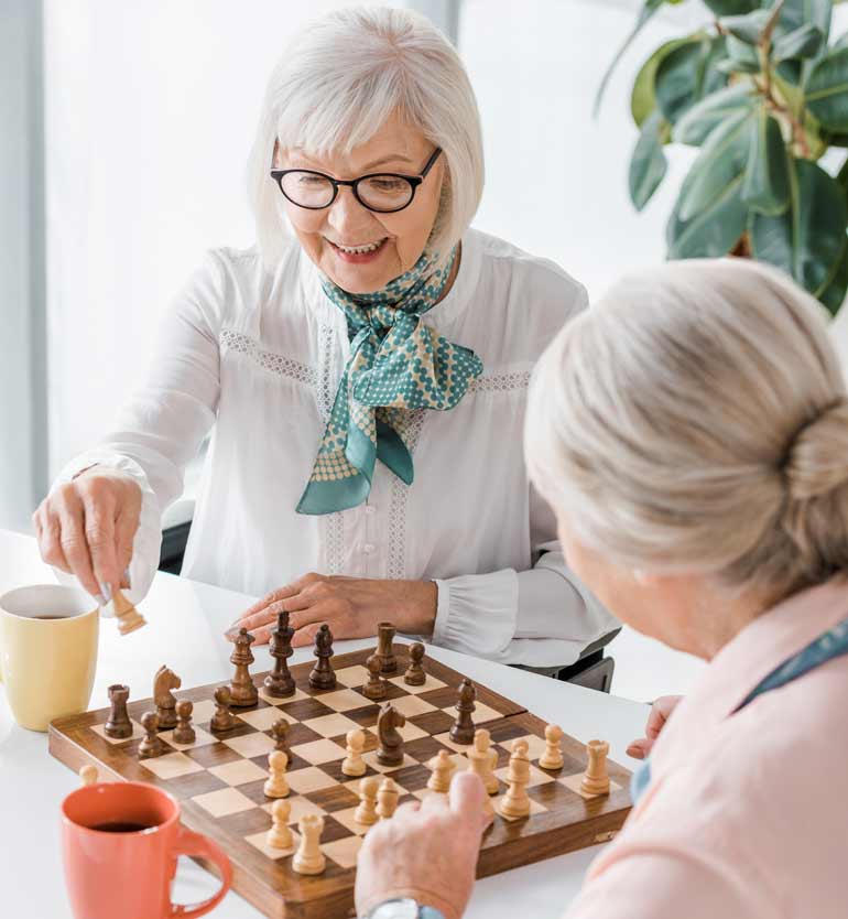 Elderly women enjoying a chess game together at a table with coffee cups nearby.