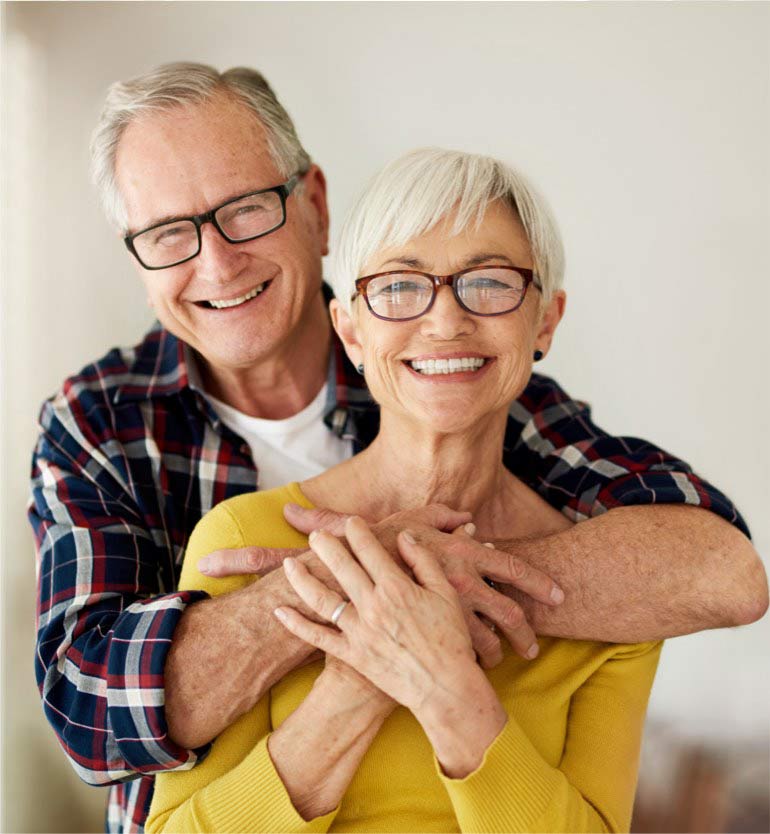 Happy senior couple hugging and smiling at the camera wearing glasses together.