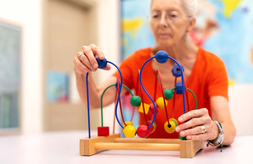 Senior woman engaged in a memory care activity with a bead maze for cognitive stimulation.